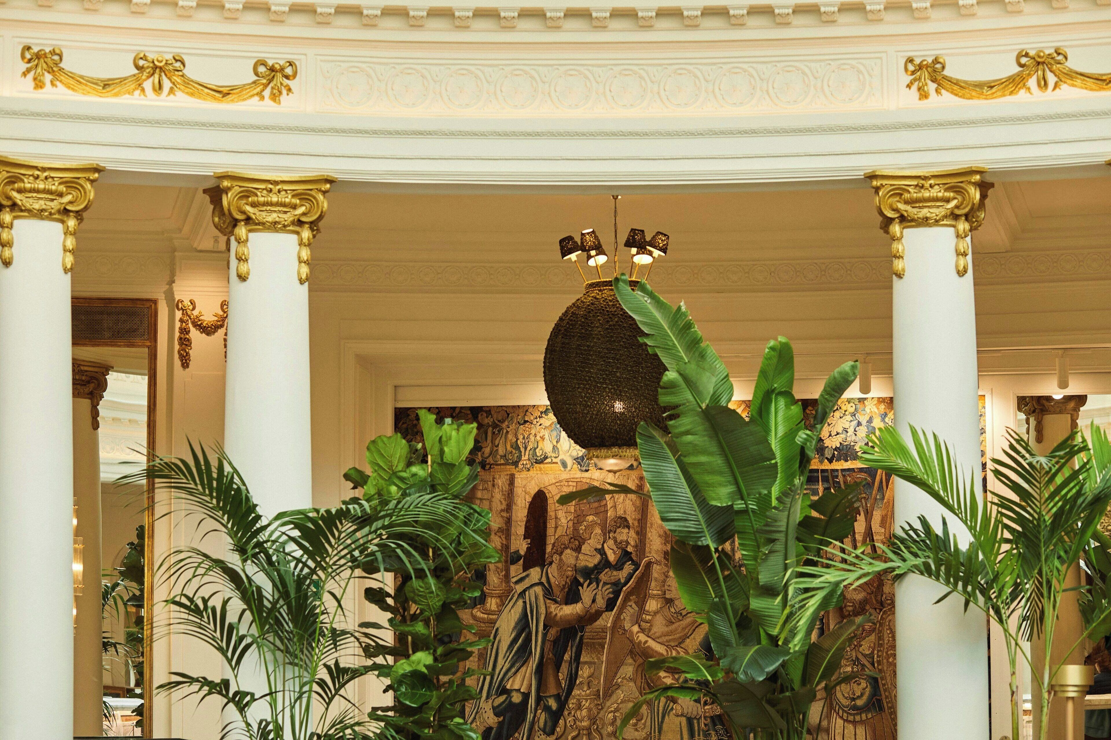 Un lobby espacioso con columnas ornamentales, un techo decorativo imponente y exuberantes plantas tropicales.