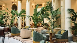 Un vestíbulo espacioso con techos altos, columnas ornamentadas y exuberante vegetación.