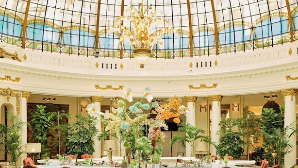 Un amplio vestíbulo con un techo abovedado, candelabros ornamentales y un arreglo floral central.