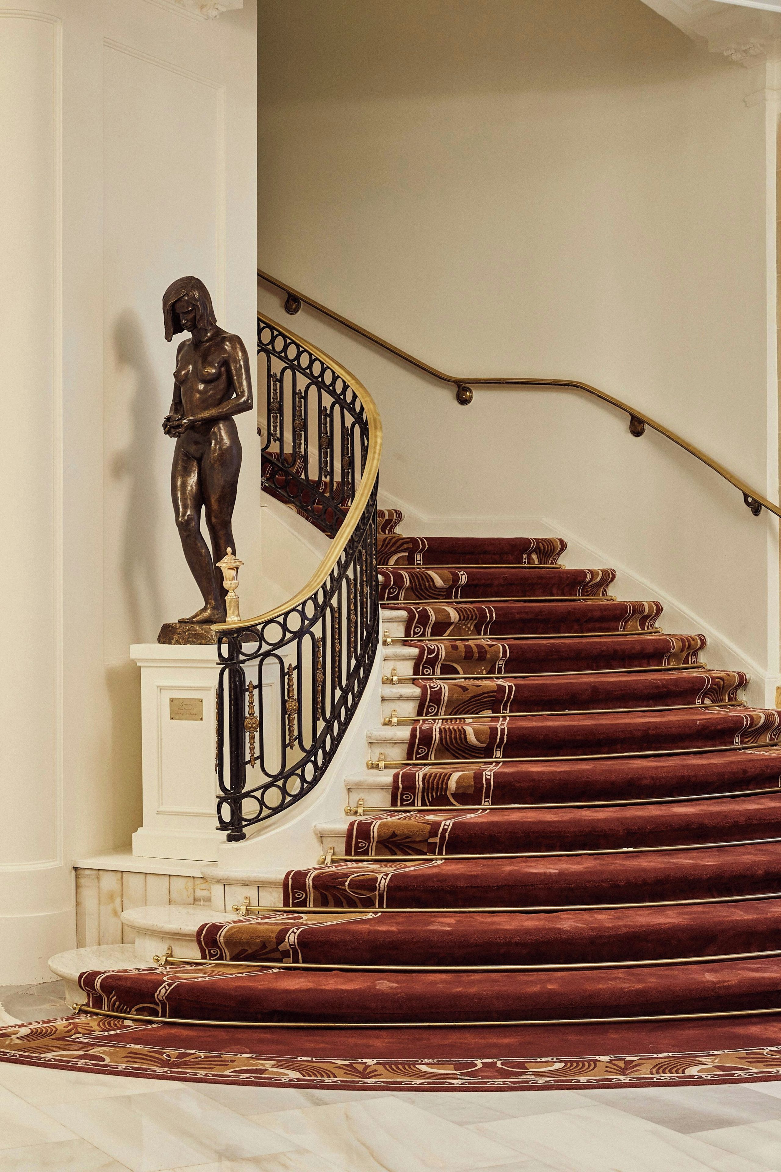 A grand staircase with a statue at the top, ornate metal railings, and patterned carpet.