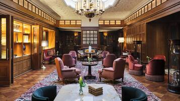 Eine großzügige Lobby mit hoher Decke, verzierten Kronleuchtern und einem runden Tisch in der Mitte, umgeben von bequemen Ohrensesseln.