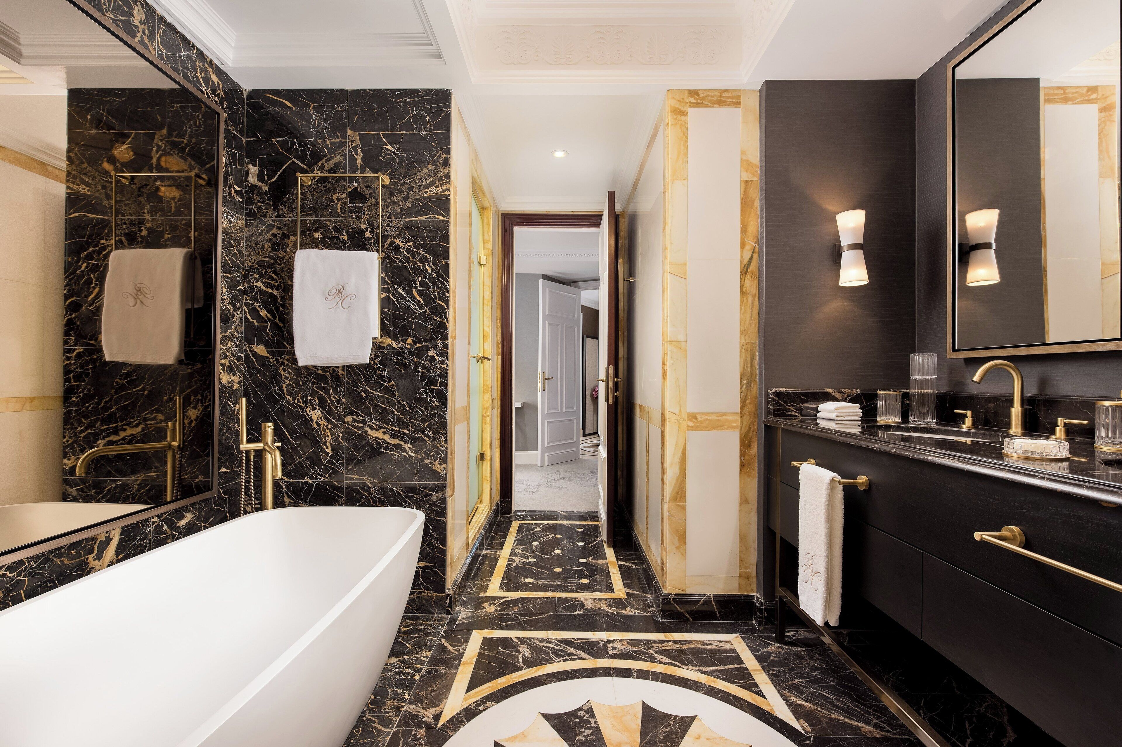 A modern bathroom with a marble floor, a bathtub, a vanity with a large mirror, and a towel rack.