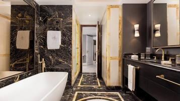 A modern bathroom with a marble floor, a bathtub, a vanity with a large mirror, and a towel rack.