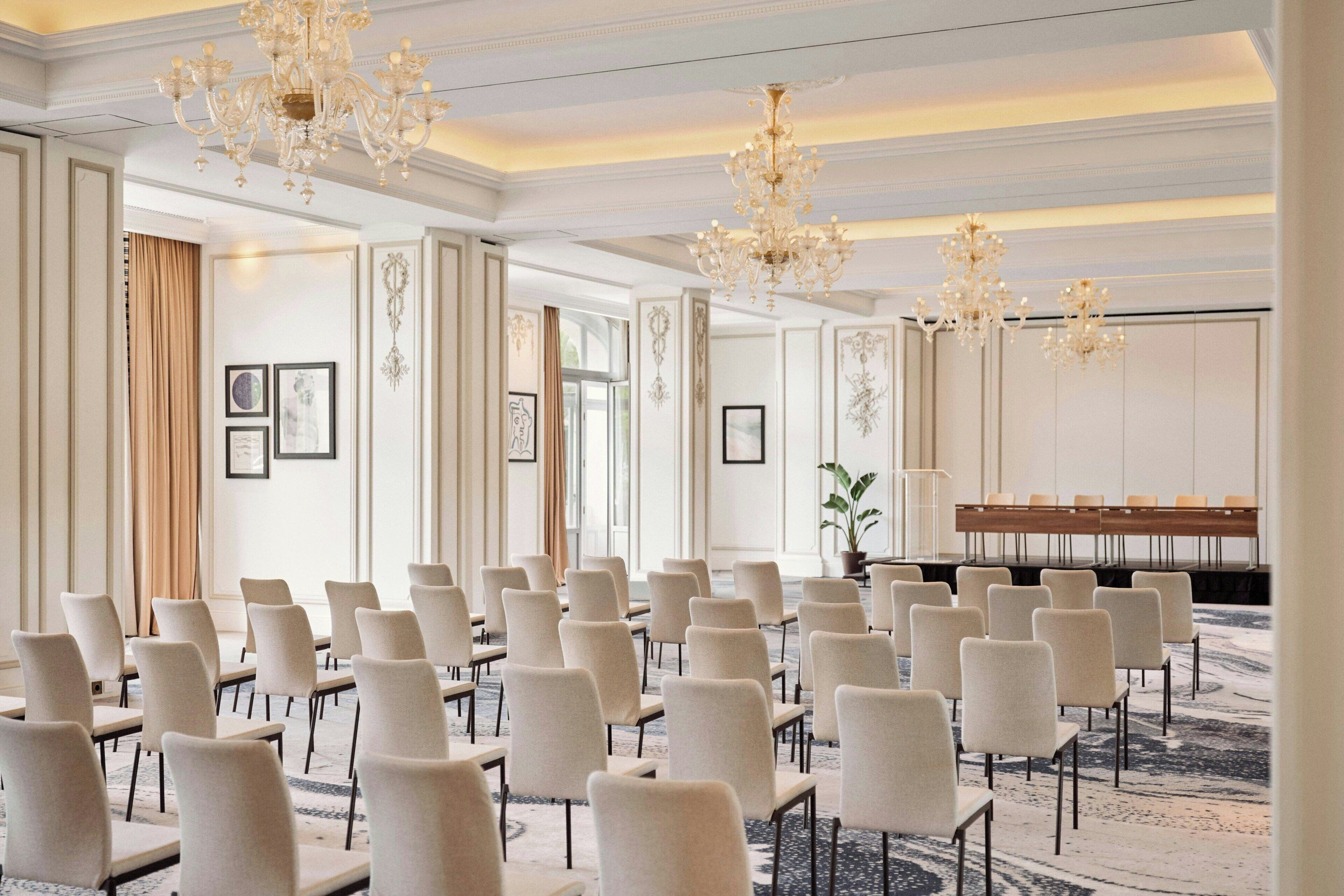 A conference room with rows of chairs, a long table, and chandeliers.