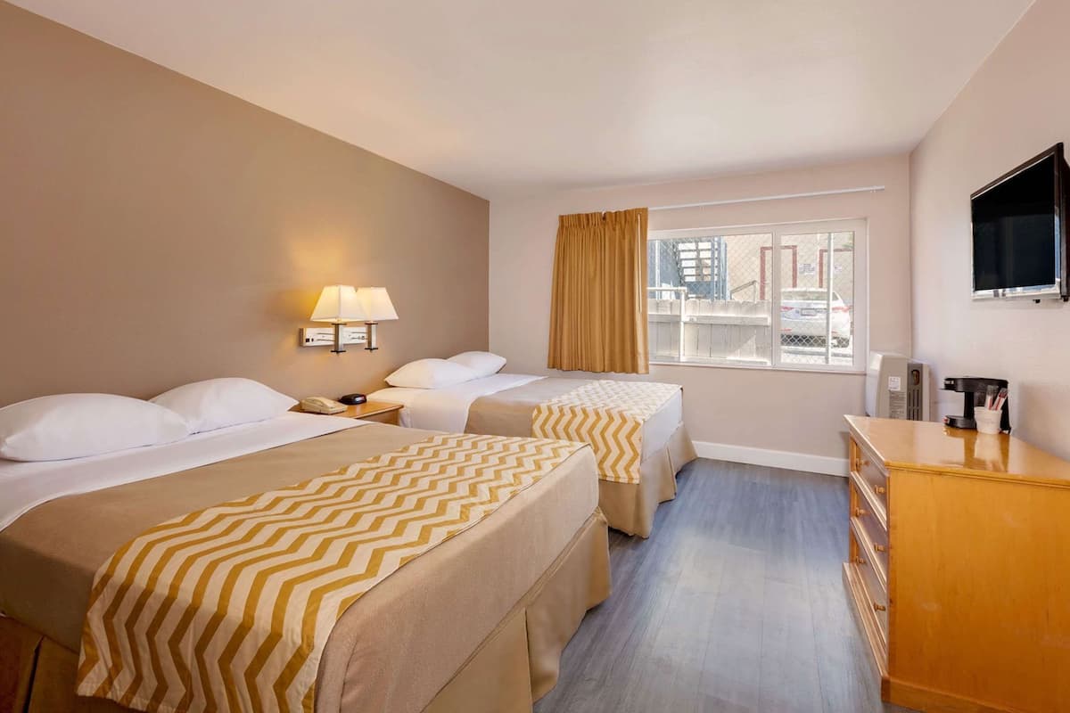 A hotel room with two beds, a desk, a TV, and a window with a view of the city.