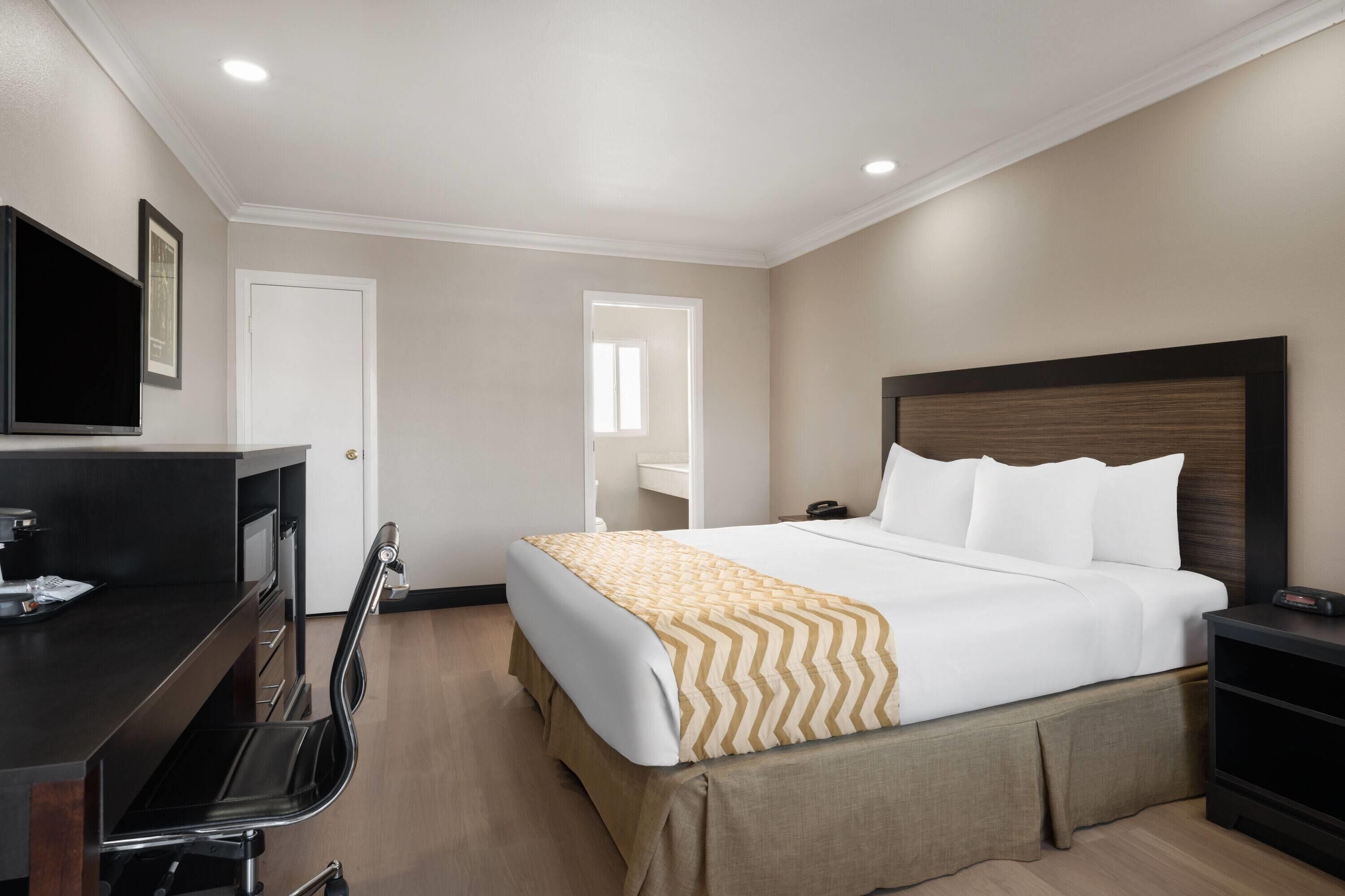 A hotel room with a bed, a desk, a chair, a television, and a door.