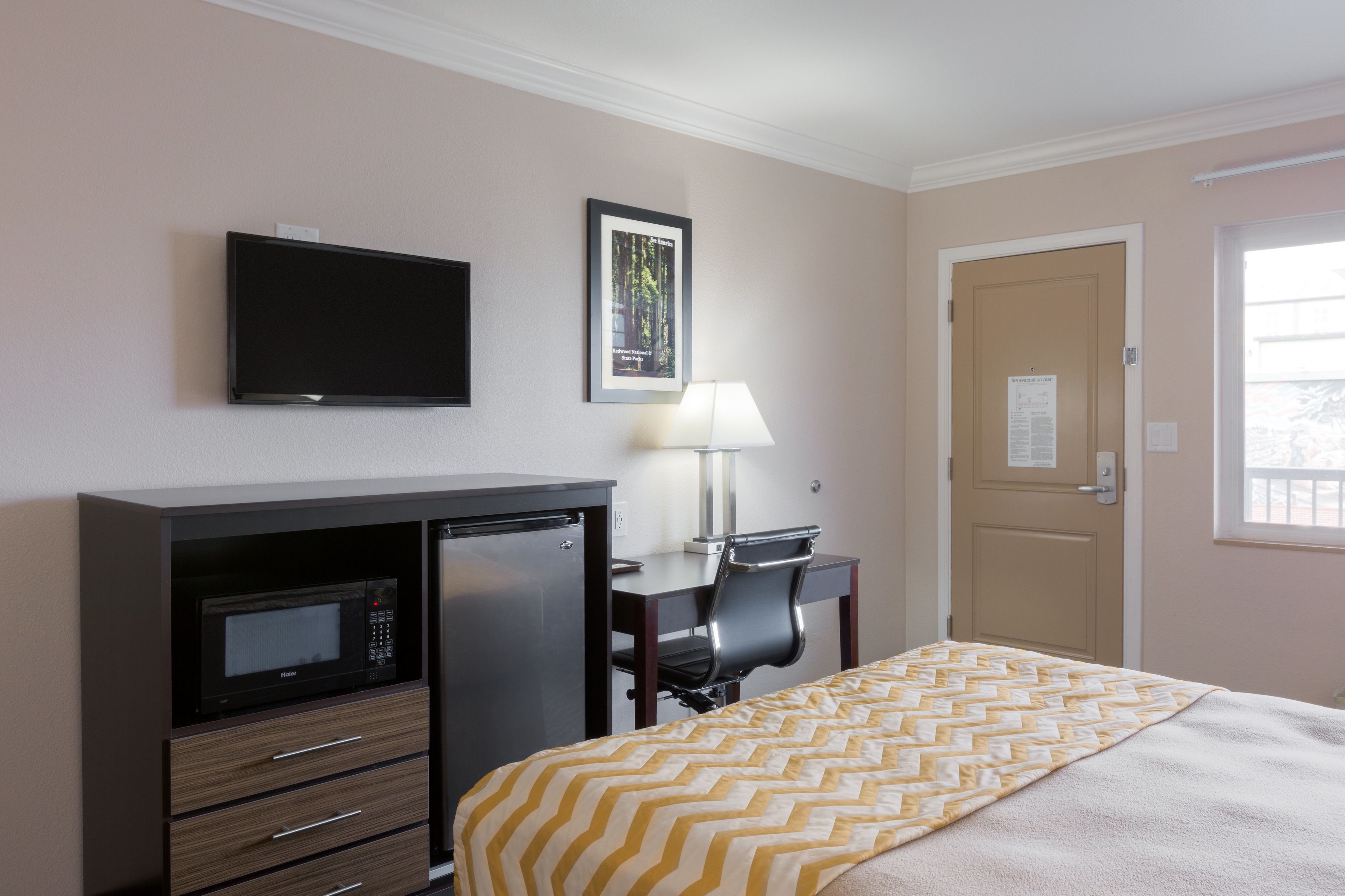 Habitación de hotel con cama, escritorio con lámpara, microondas y televisión.