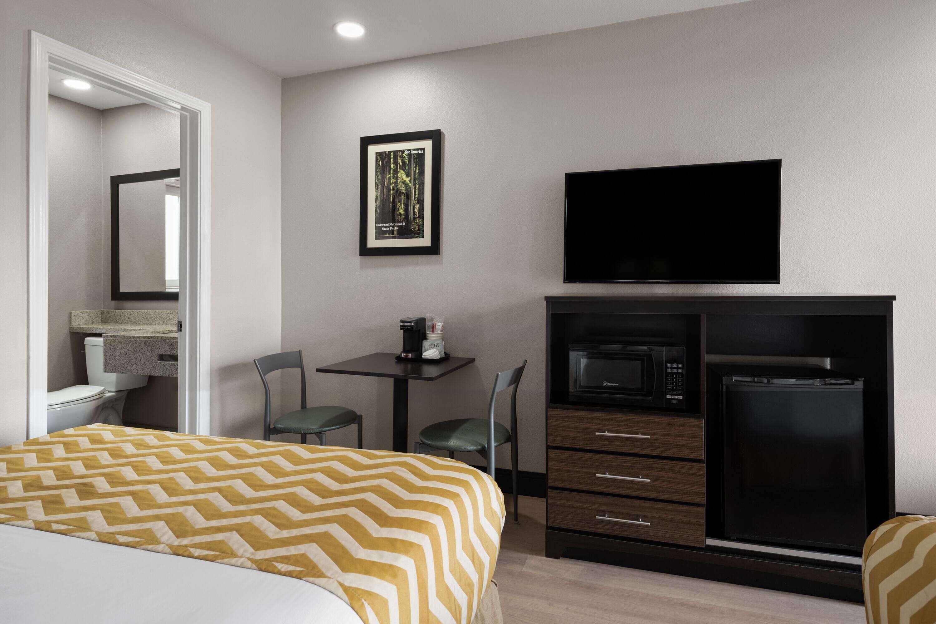 A hotel room with a bed, a desk with a chair, a television, a microwave, and a refrigerator.