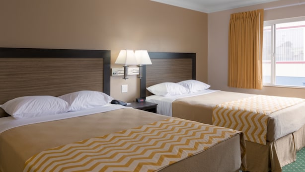 Une chambre d’hôtel avec deux lits, une table de chevet, une lampe et une fenêtre avec des rideaux.
