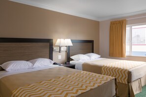 Une chambre d’hôtel avec deux lits, une table de chevet, une lampe et une fenêtre avec des rideaux.