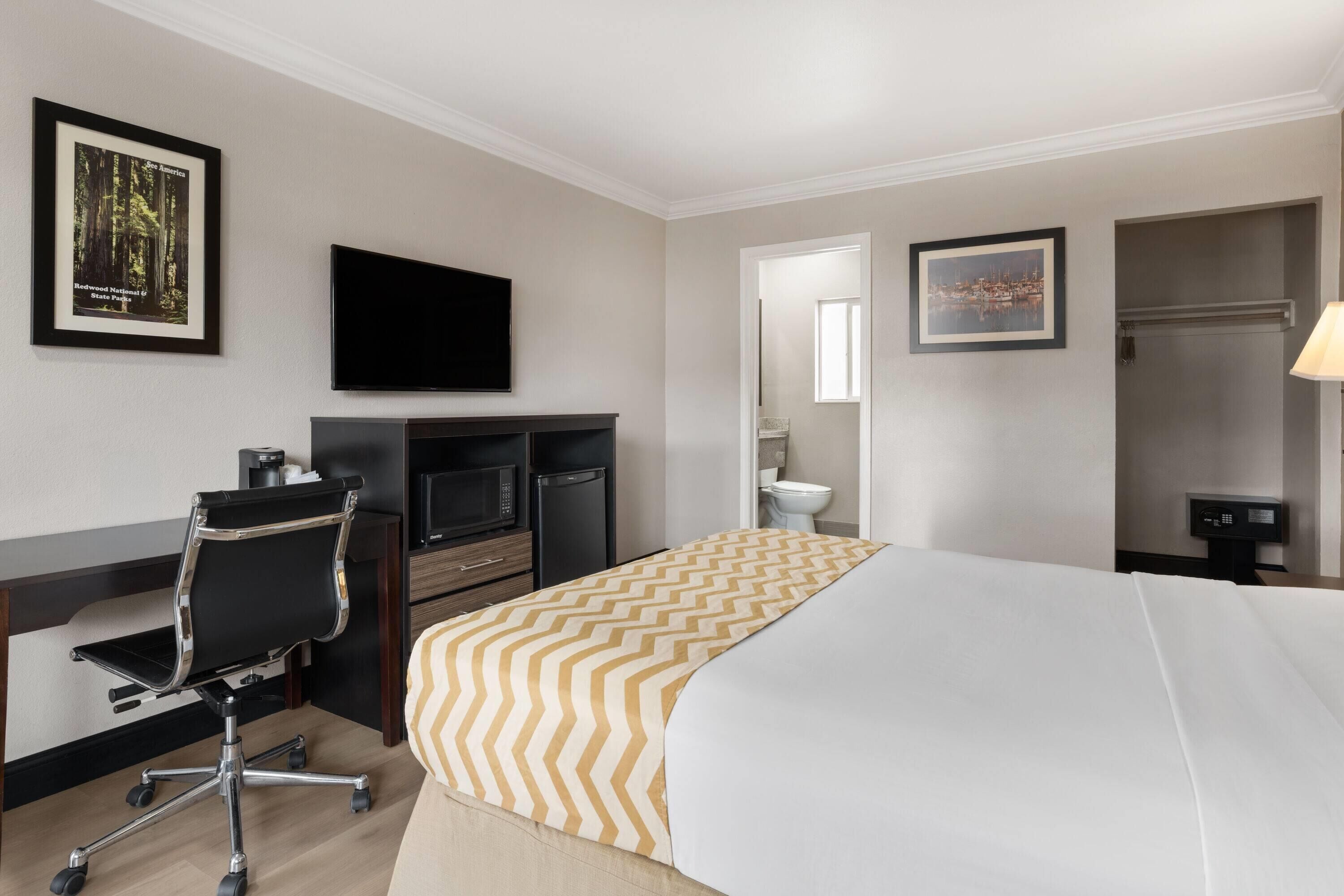 A hotel room with a bed, desk, chair, television, and a bathroom.