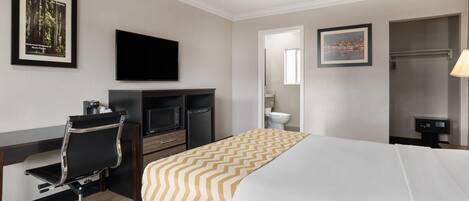 A hotel room with a bed, desk, chair, television, and a bathroom.