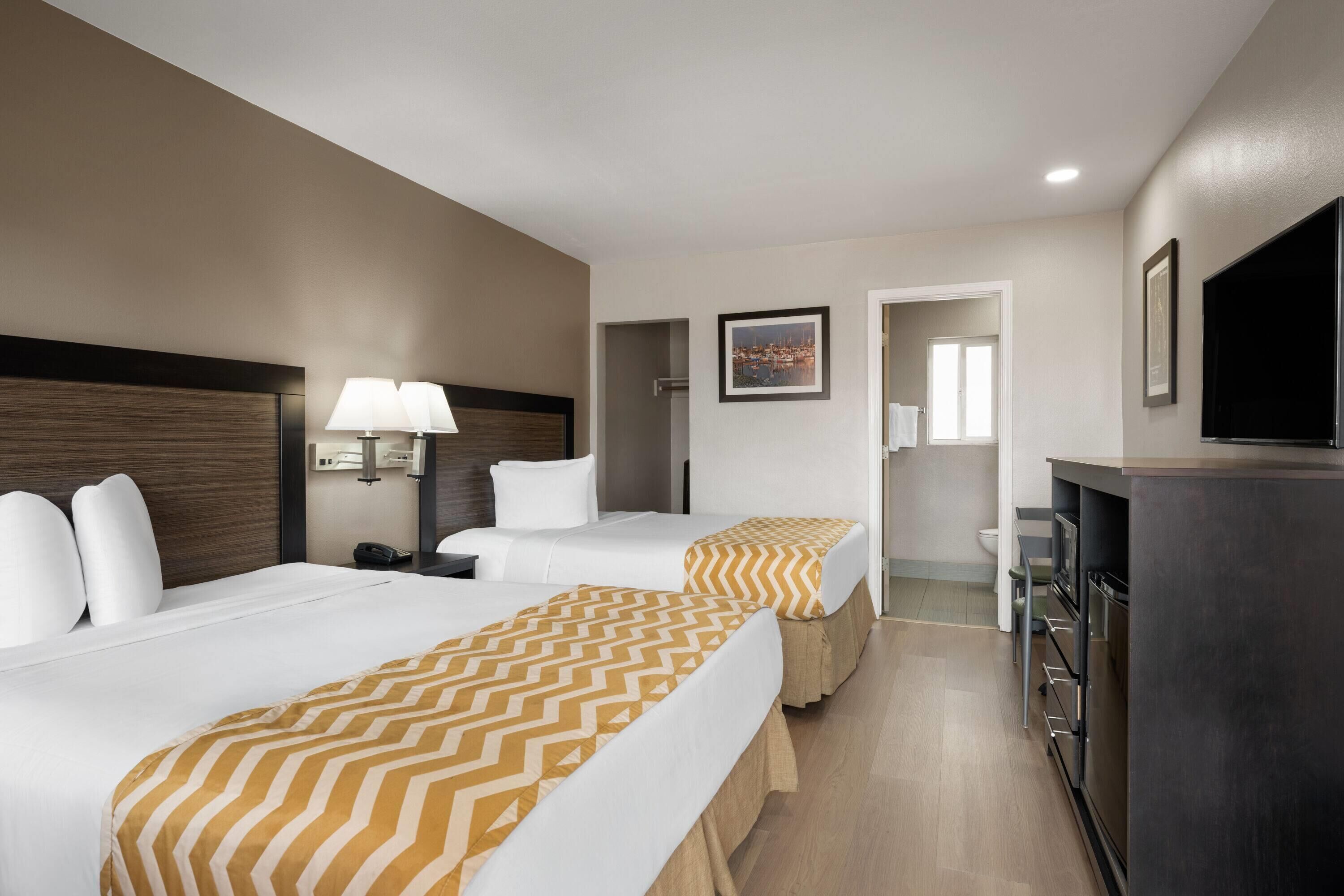 A hotel room with two beds, a desk, a TV, and a bathroom.