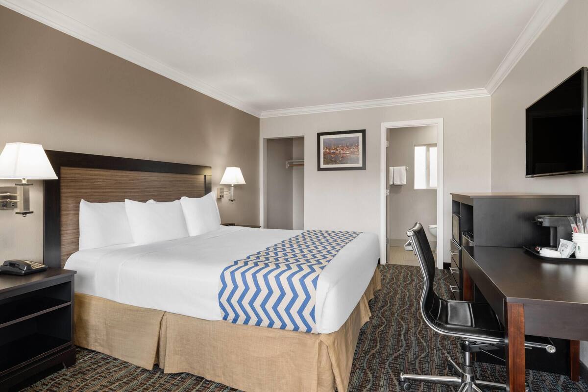 A hotel room with a bed, bedside lamps, a desk with a chair, a television, and a coffee maker.