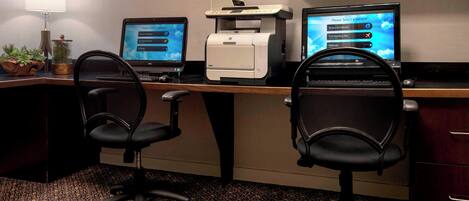 A workspace with two computer monitors, a printer, and two office chairs.
