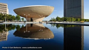 A modern building with a unique bowl-like structure, a reflective pool in front, and a tall skyscraper in the background. - Marriott Albany (Albany)