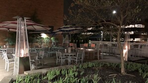 An outdoor patio area with tables and chairs, a fire pit, and umbrellas providing shade. - Marriott Albany (Albany)