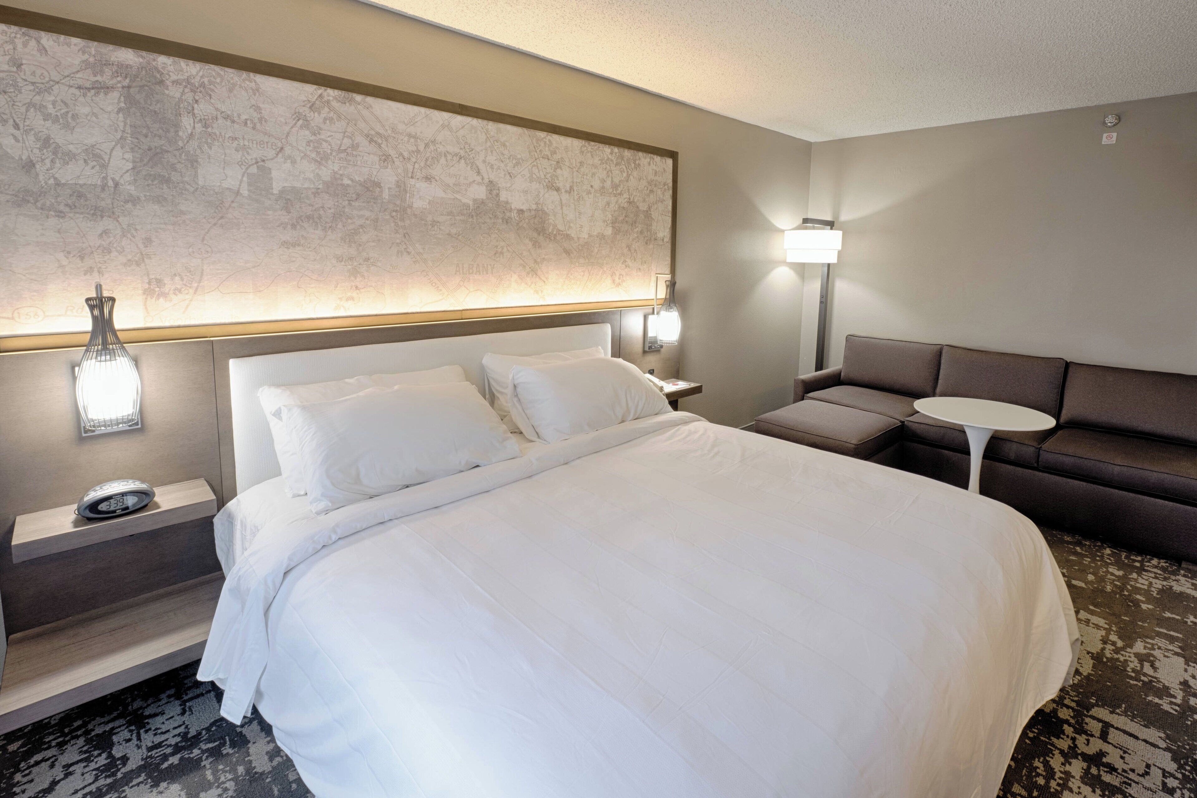 A hotel room with a large bed, a sofa, a small table, and a wall map.