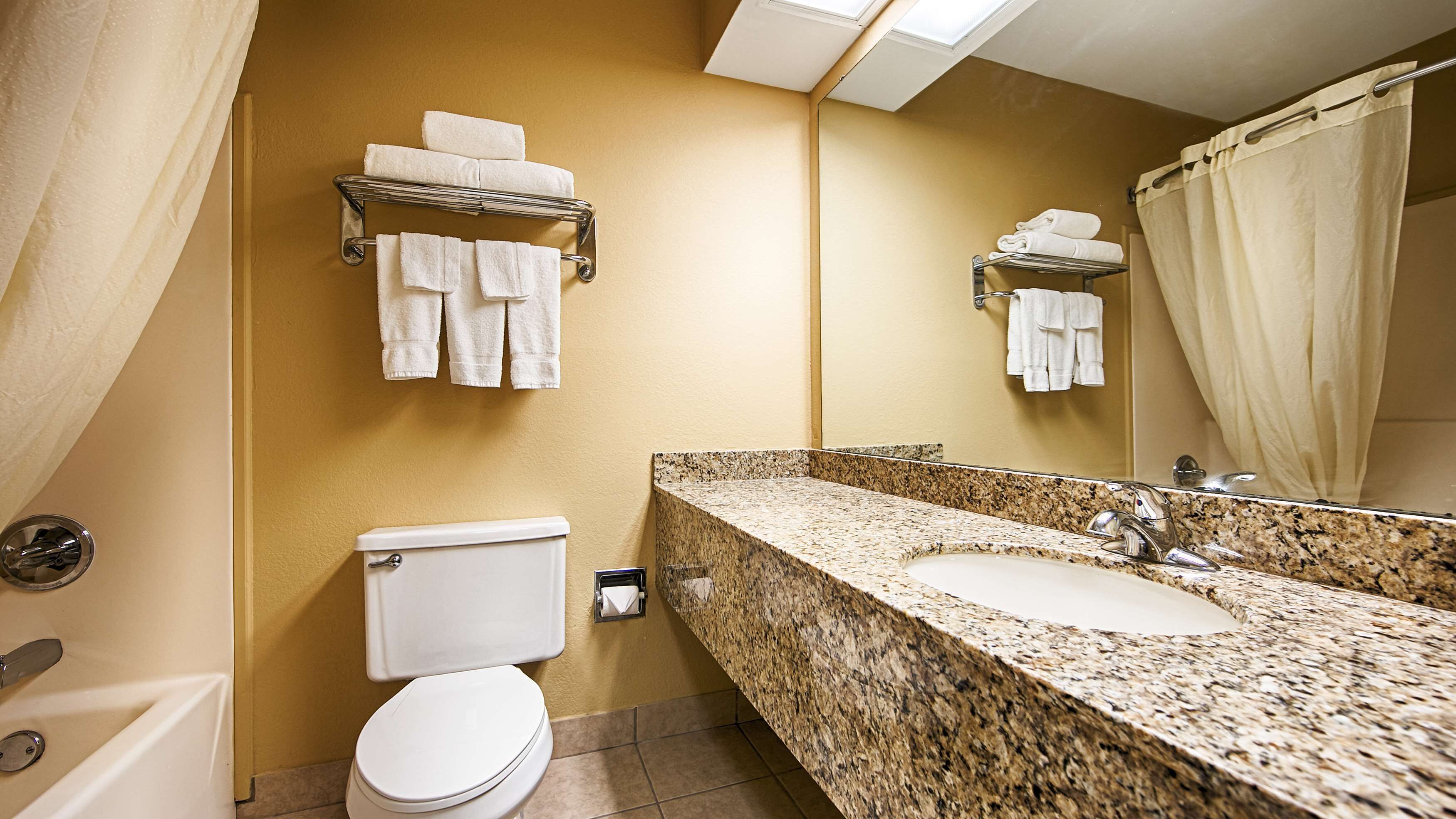 A bathroom with a granite countertop sink, a toilet, and towel racks on the wall.