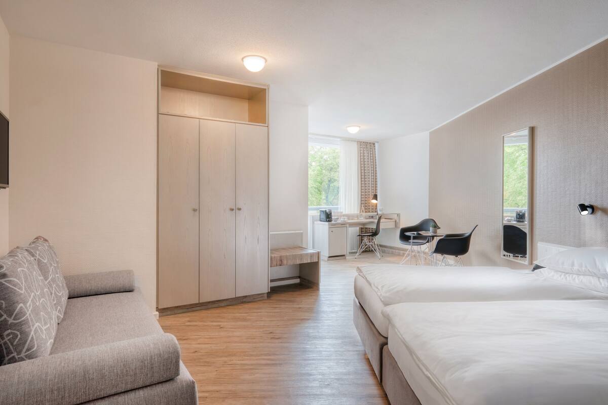 Un dormitorio moderno con cama, escritorio y silla. Hay un armario y un sofá.
