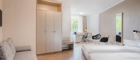 A modern bedroom with a bed, a desk, and a chair. There is a wardrobe and a sofa.