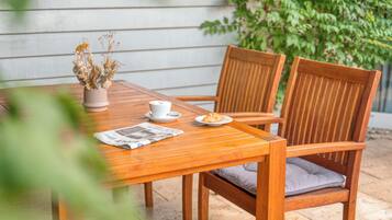 A wooden table with a newspaper, a white cup, and a plate with a pastry.