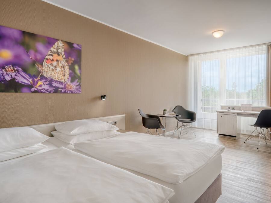 A hotel room with two beds, a desk, two chairs, a small table, and a window with curtains.