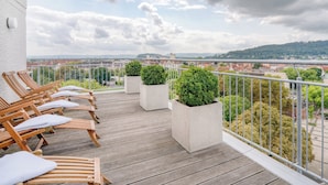 A balcony with wooden lounge chairs and potted plants, overlooking a cityscape with buildings and a distant hill. - Parkhotel Hameln (Hamelin)