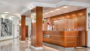 A modern reception area with a wooden reception desk, a large abstract painting on the wall, and a polished tiled floor. - Parkhotel Hameln (Hamelin)
