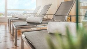 A spa area with reclining chairs and towels, large windows, and a view of the city. - Parkhotel Hameln (Hamelin)