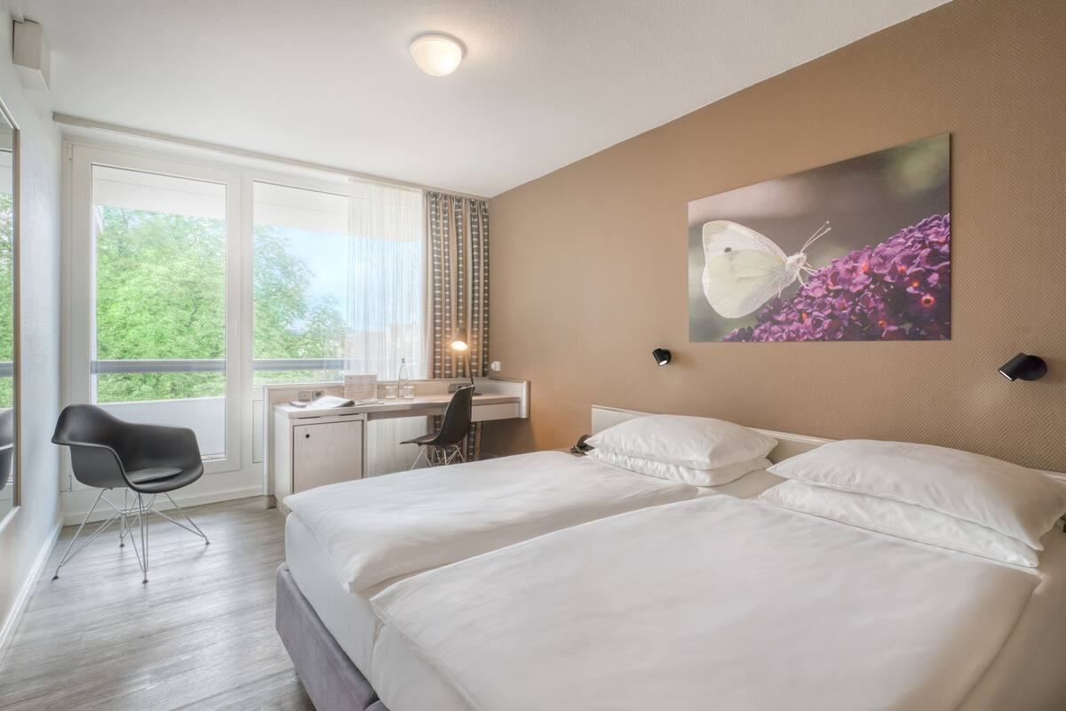 Una habitación de hotel con una cama grande, un escritorio, una silla y una ventana con cortinas.
