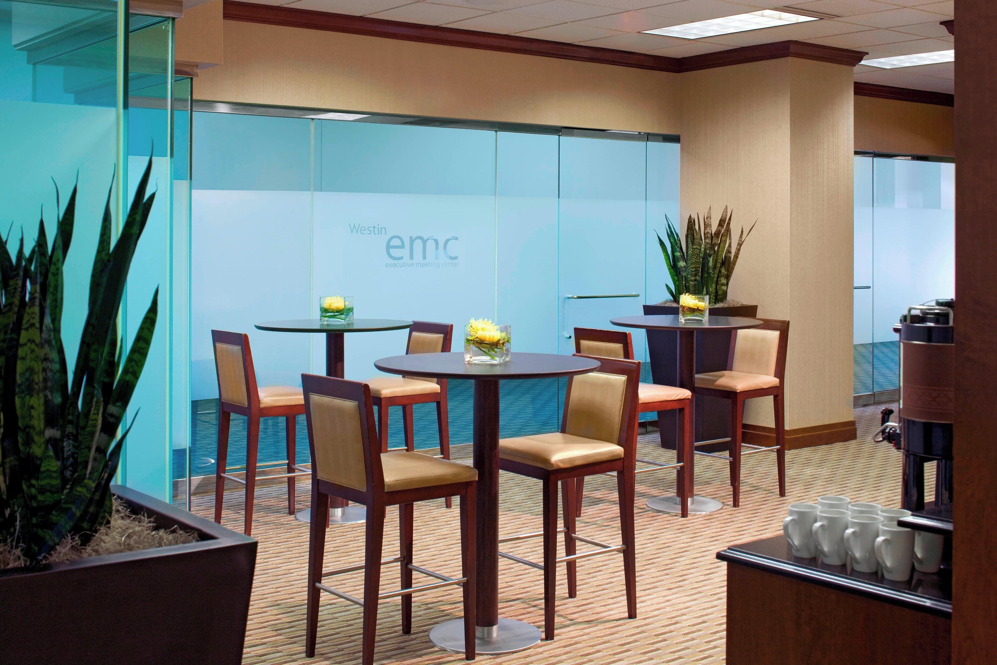 A Westin Executive Meeting Center with round tables and chairs, a coffee station, and a view of the ocean through the glass wall.