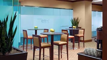 A Westin Executive Meeting Center with round tables and chairs, a coffee station, and a view of the ocean through the glass wall.