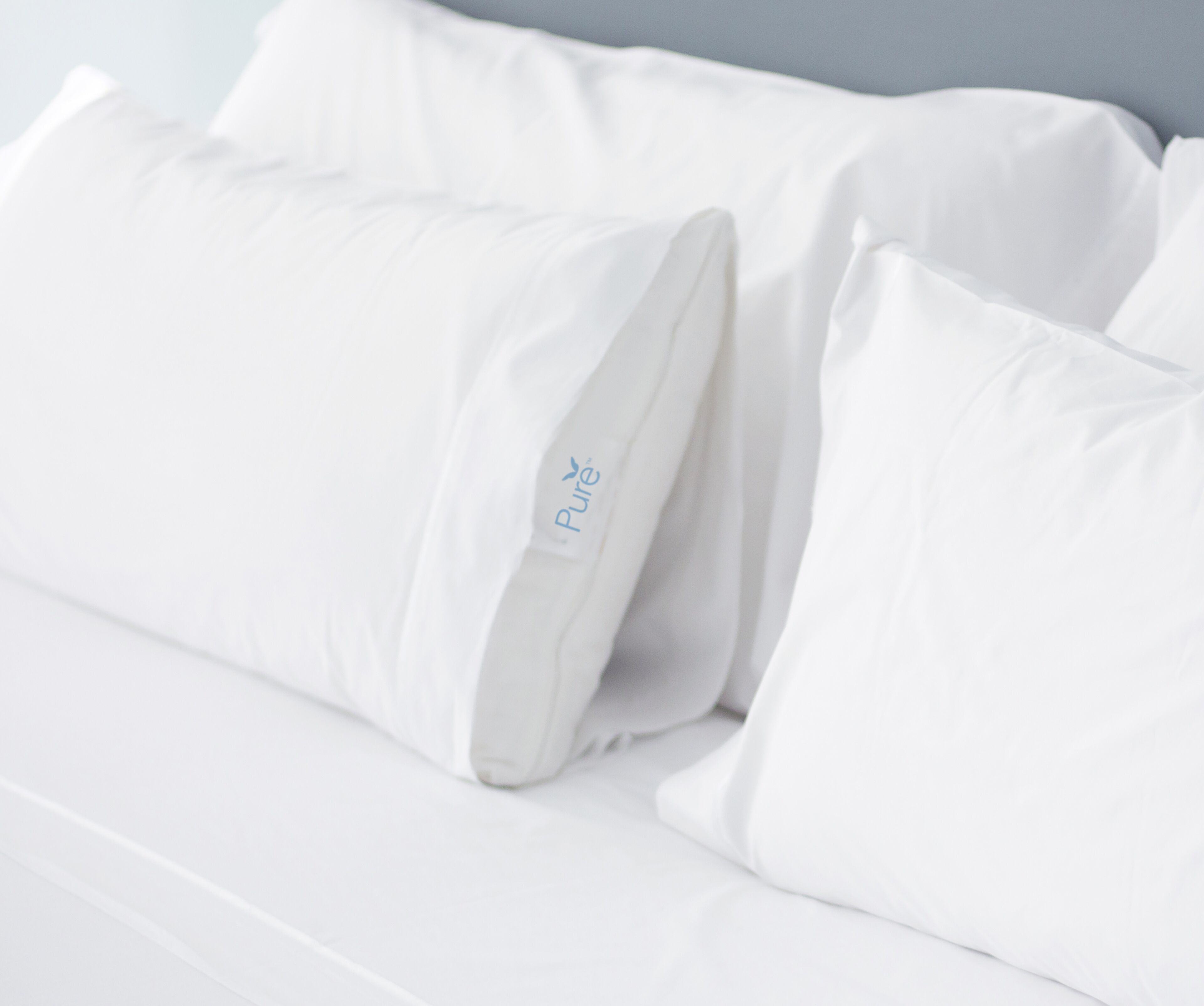 Una cama con ropa de cama y almohadas blancas, una de ellas con el logo 'Pure'.