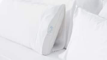 Una cama con ropa de cama y almohadas blancas, una de ellas con el logo 'Pure'.