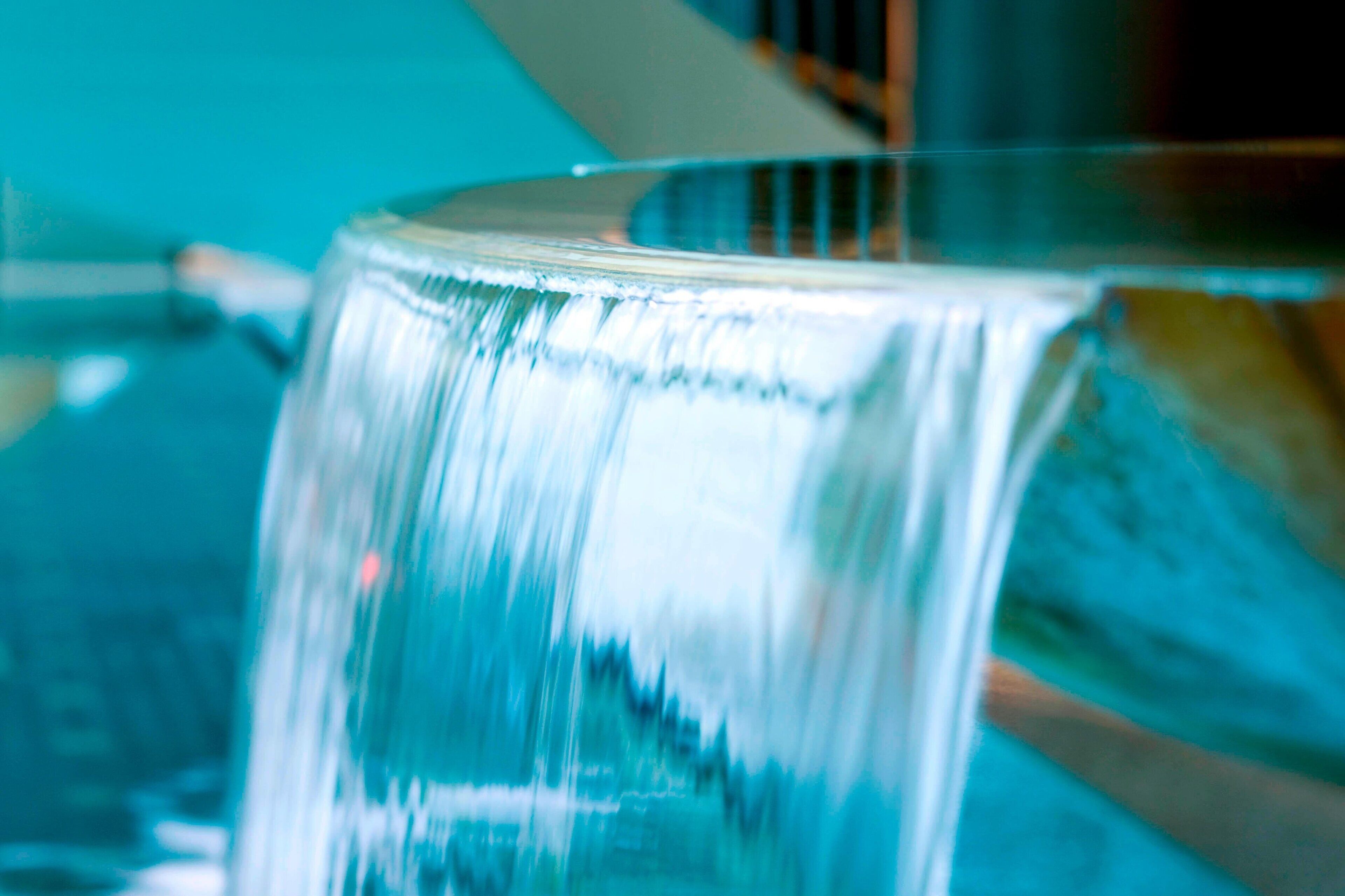 Un gros plan d’une fontaine d’eau en verre transparent, dotée d’une base métallique, qui reflète la lumière et crée un effet scintillant.