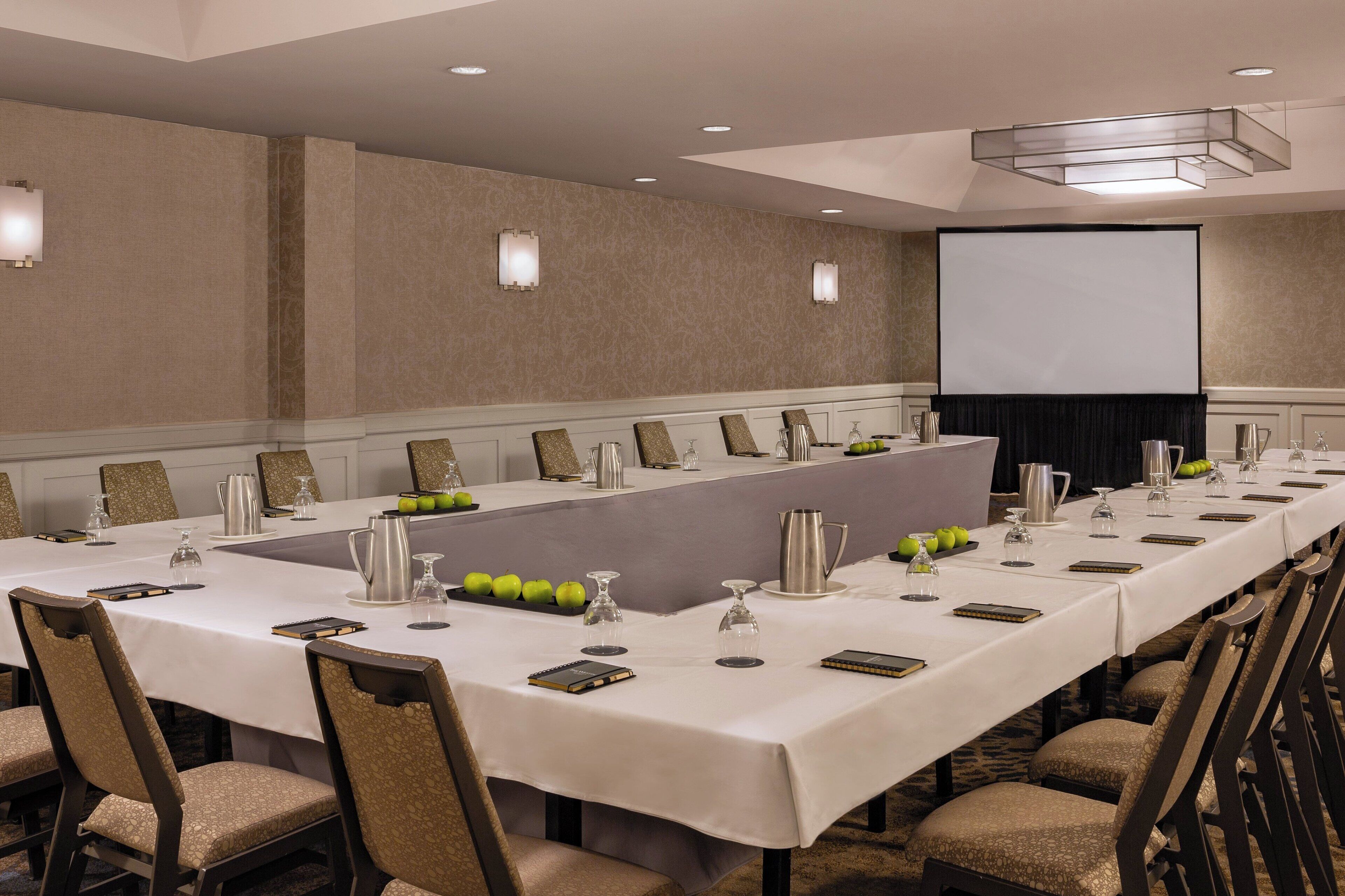 A conference room with a long table, chairs, a projector screen, and a whiteboard.