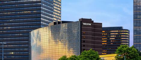 Un immeuble moderne de grande hauteur, doté d’une façade en verre, d’une enseigne « WESTIN » bien visible et d’une structure incurvée adjacente.