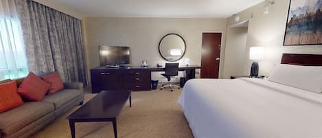 Een hotelkamer met een bed, een bureau, een televisie, een bank en een groot raam met gordijnen.