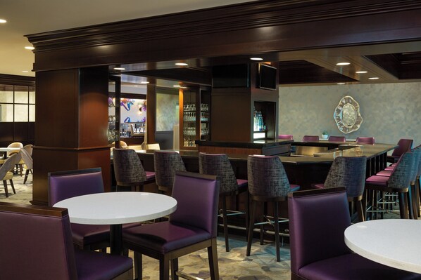 A bar area with round tables and purple chairs, a counter with a decorative mirror, and a patterned wall.