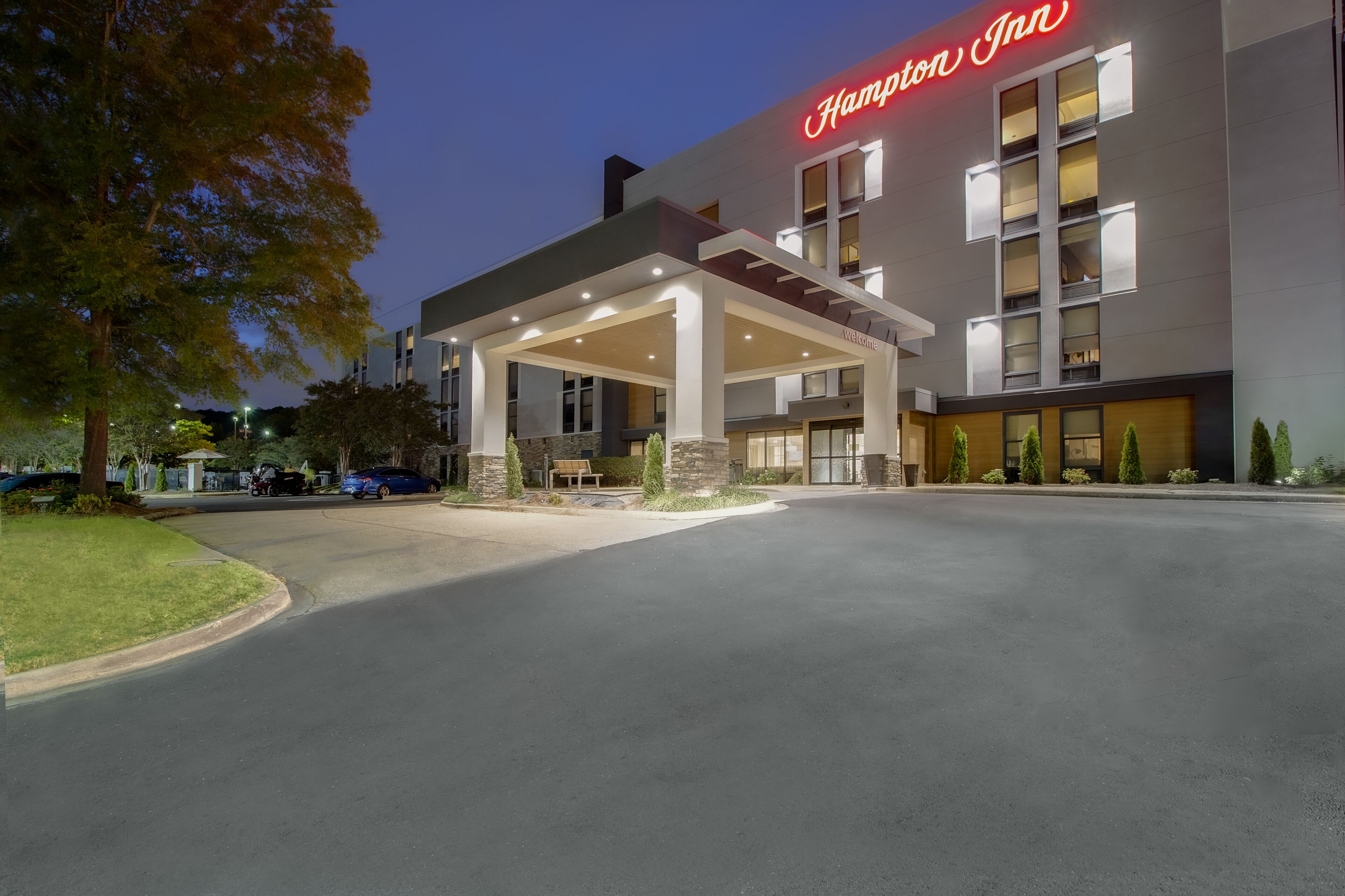 Un hotel Hampton Inn con un área exterior cubierta, una entrada bien iluminada y una vista despejada de la fachada del edificio.