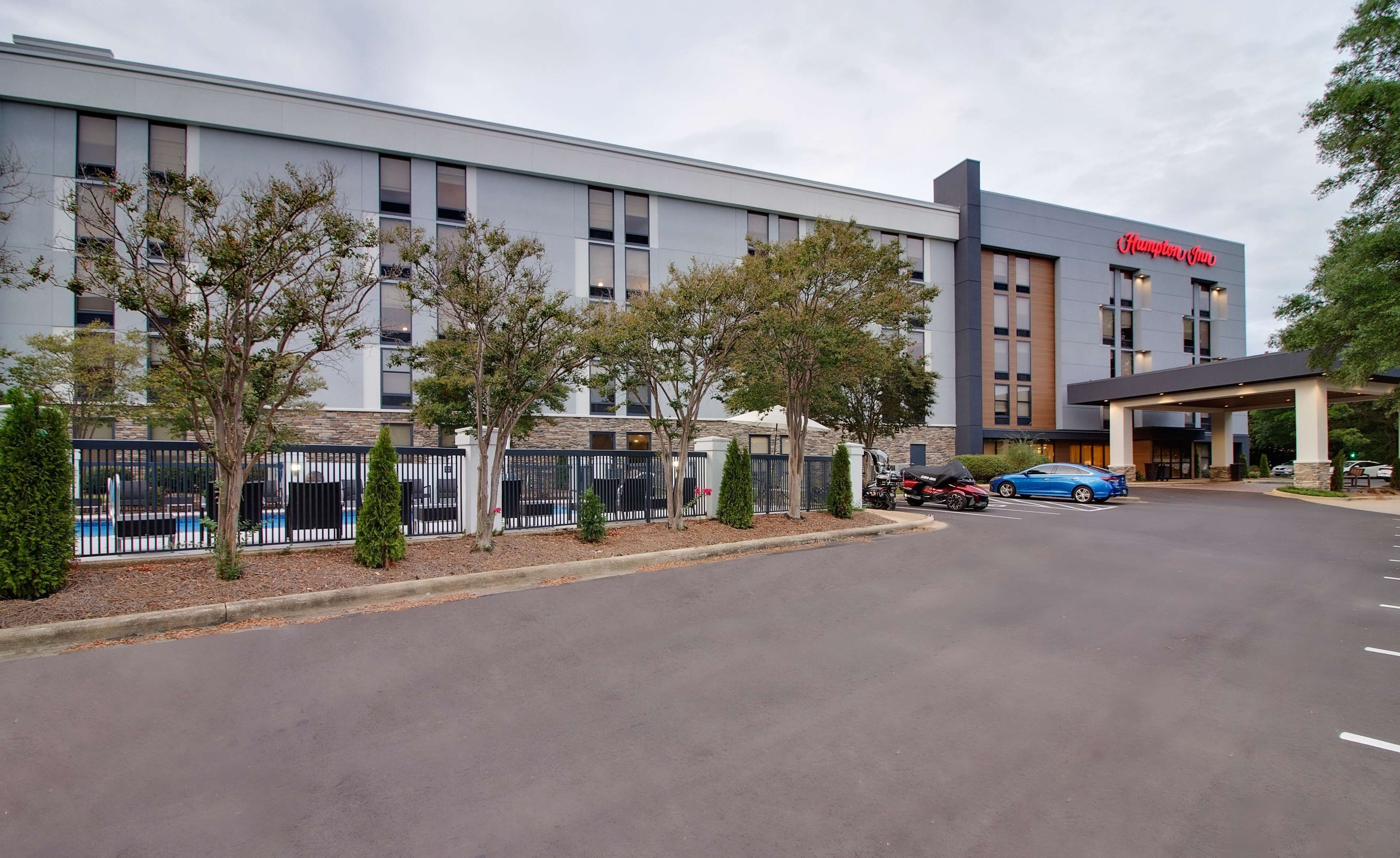 A modern hotel with a flat roof, a covered entrance, and a swimming pool area with a fence.