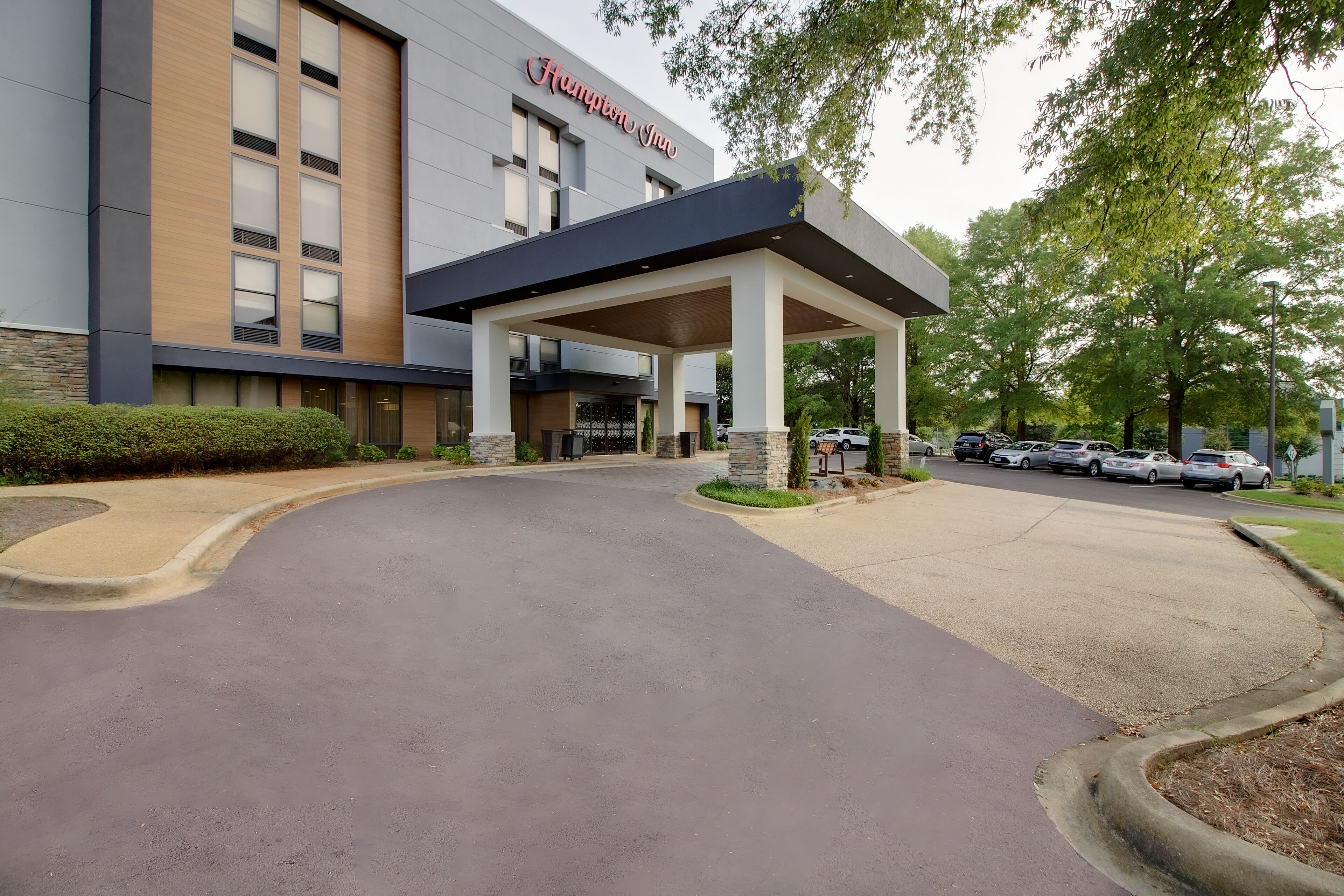 Een moderne hotelingang met een overdekte doorgang, een verharde oprit en geparkeerde auto's.