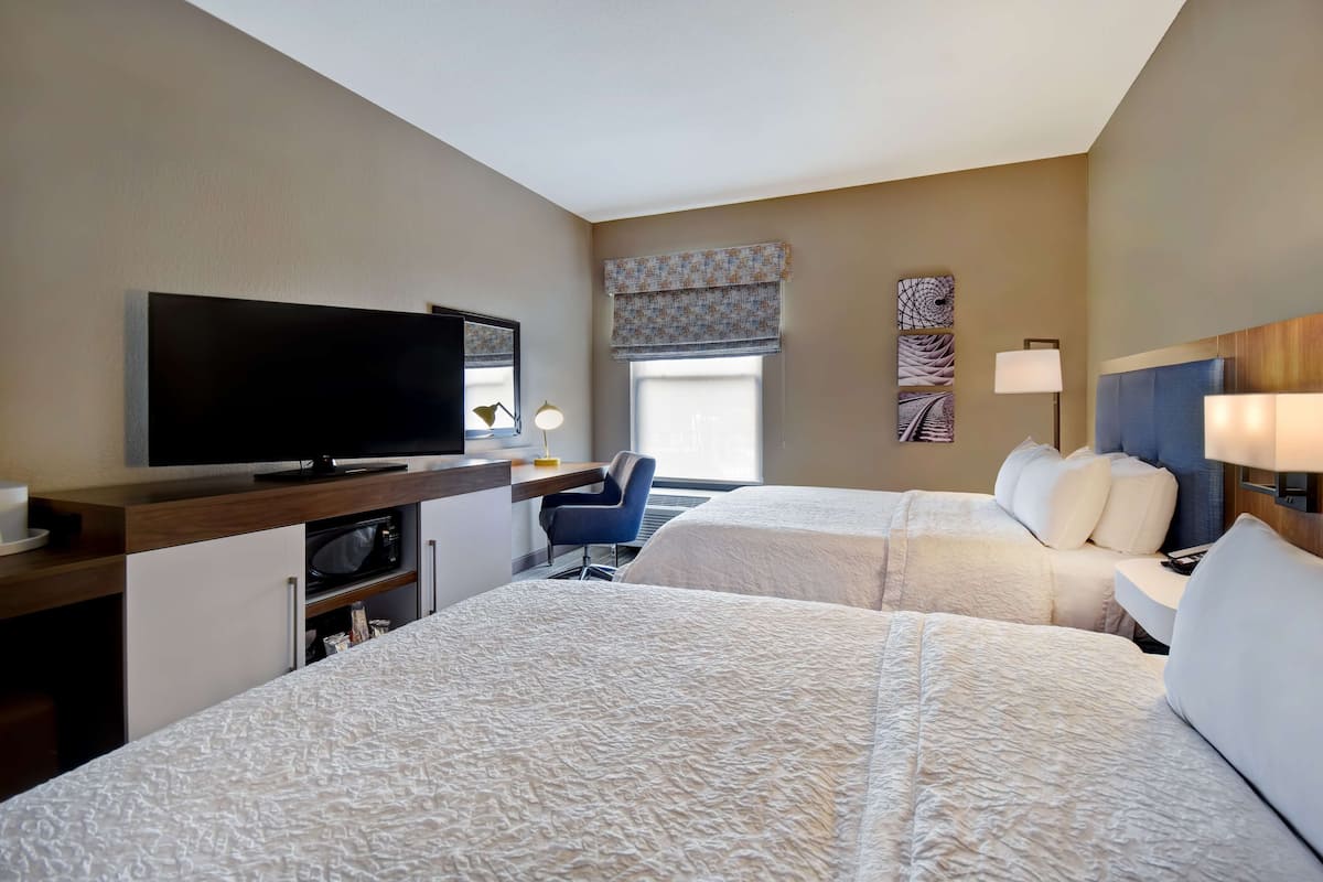 A hotel room with two beds, a TV, a desk with a lamp, and a chair.