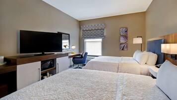 A hotel room with two beds, a TV, a desk with a lamp, and a chair.