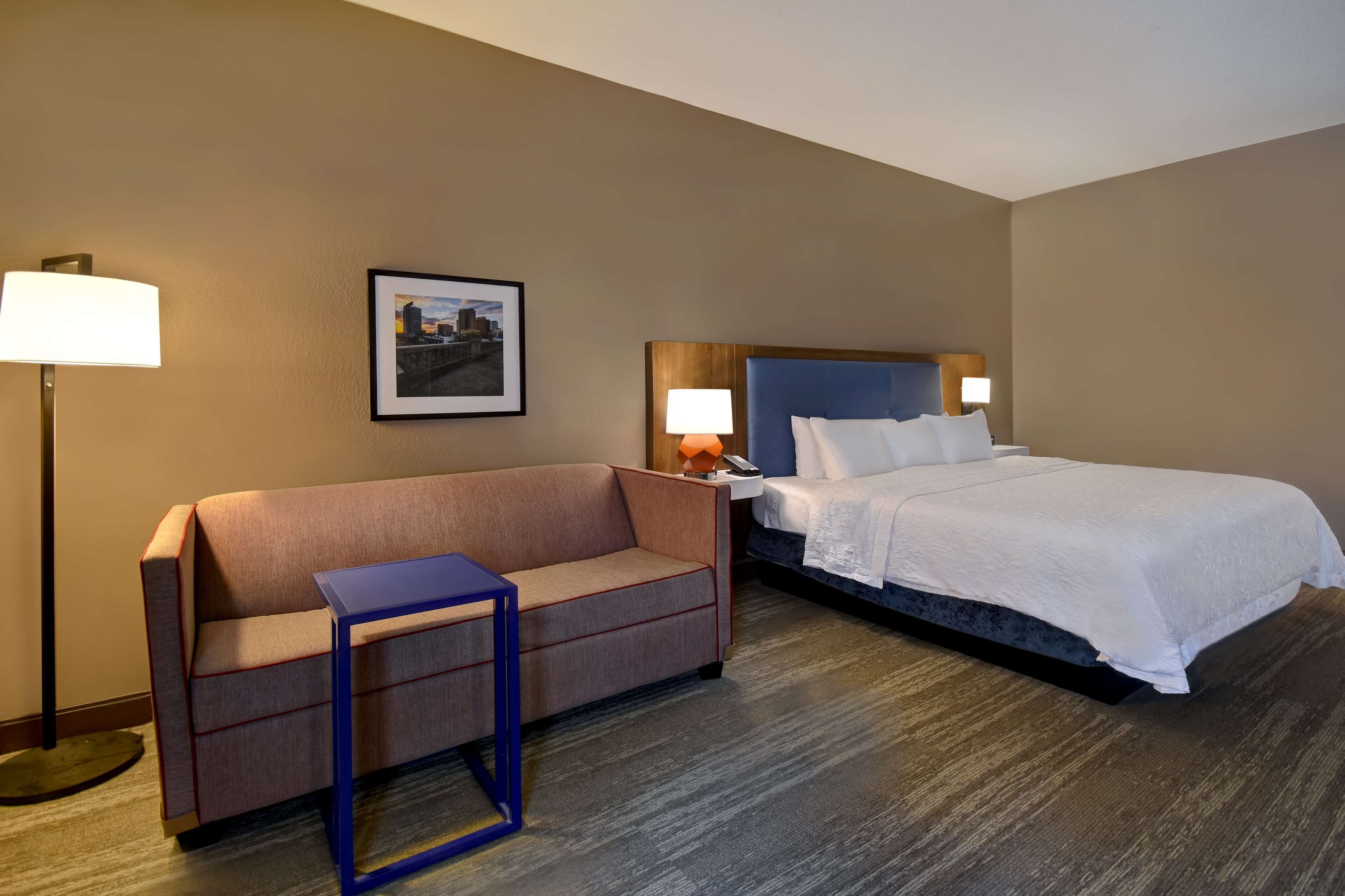 A hotel room with a bed, a sofa, a small table, and a picture on the wall.