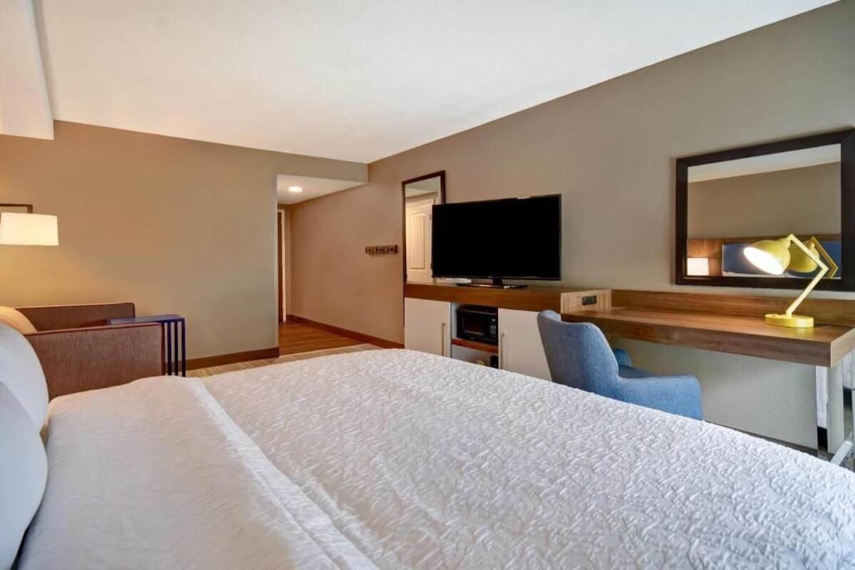 A hotel room with a bed, a desk, a television, a mirror, and a lamp.