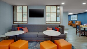 A modern lounge area with a grey sofa, orange ottomans, and a flat-screen TV mounted on the wall. - Hampton Inn Birmingham-Colonnade 280 (Birmingham)