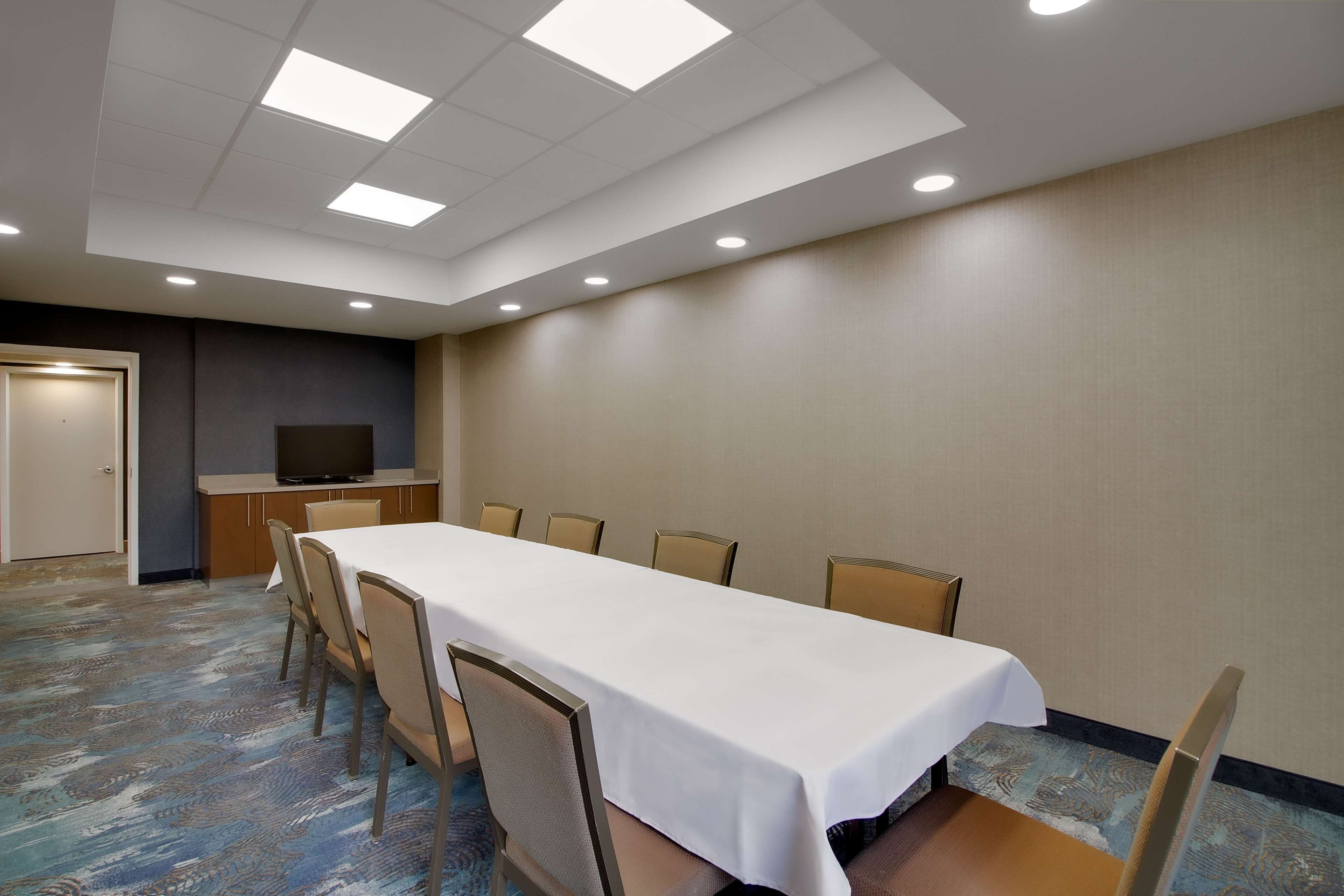 Une salle de conférence avec une longue table, des chaises, un téléviseur et une porte.