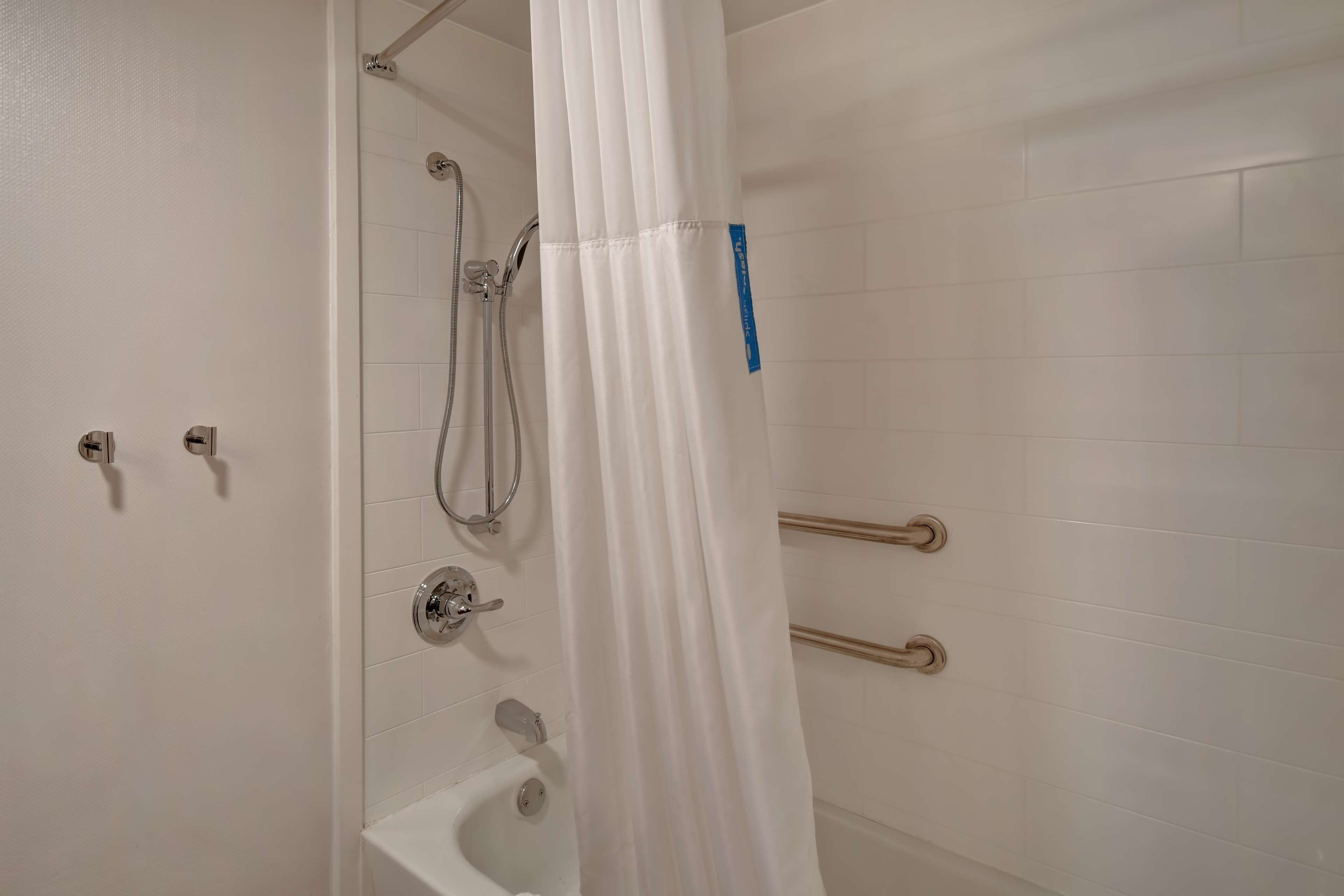 A bathroom with a shower, grab bars, and a bathtub.